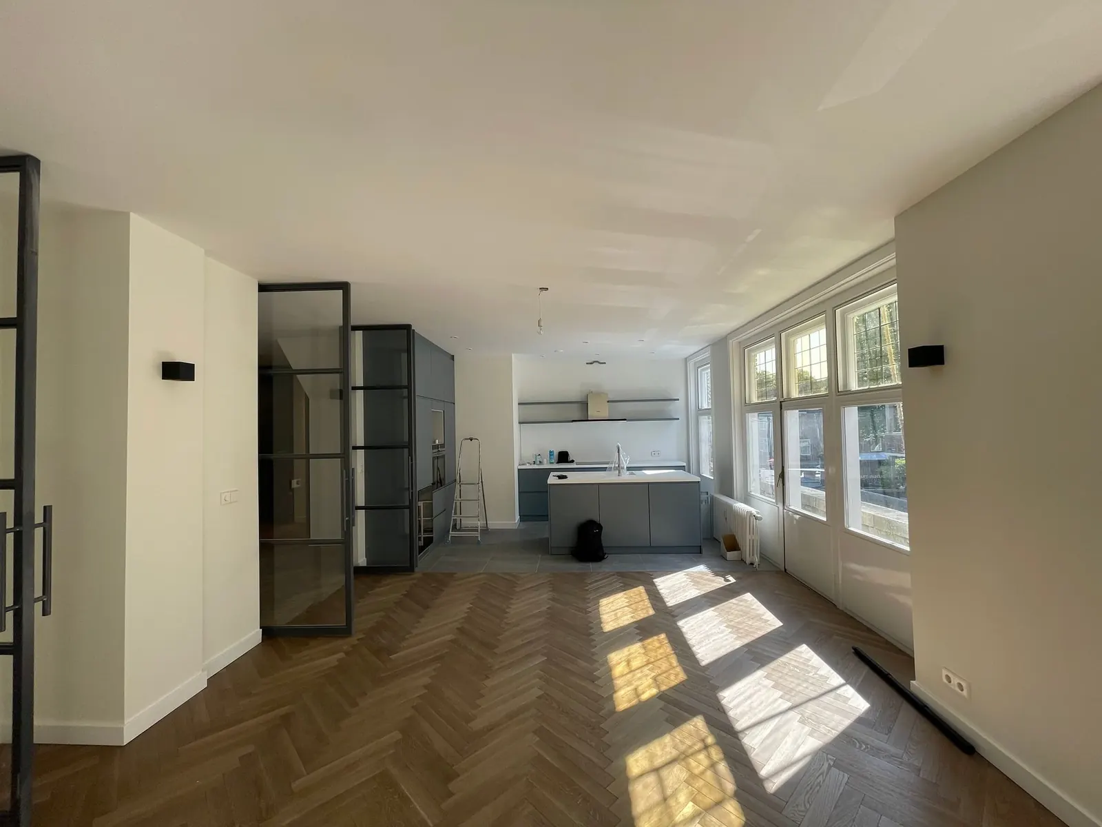Dezelfde benedenwoning na de renovatie, lichte kamer met hoge ramen